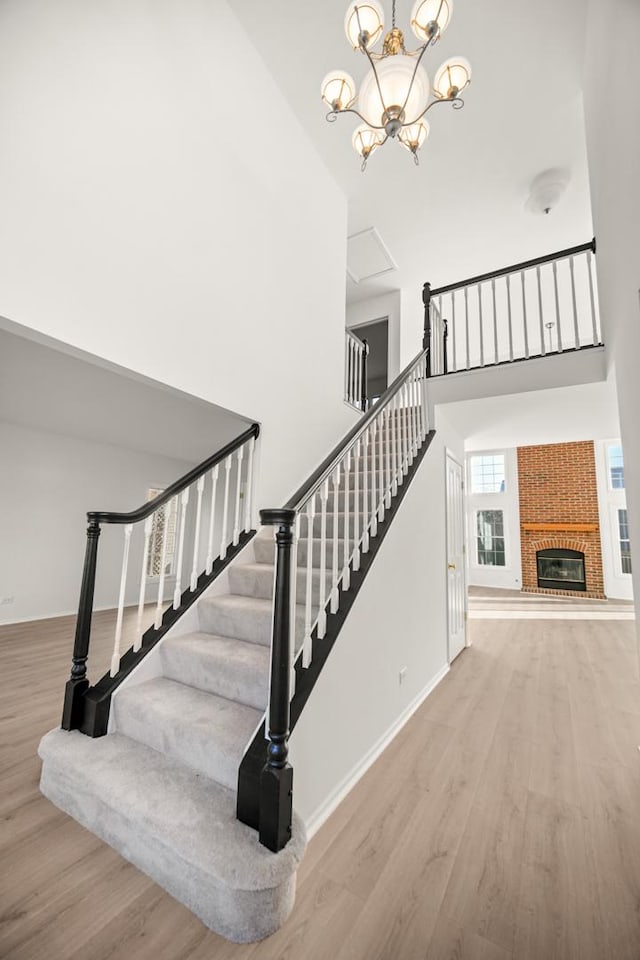 staircase with a fireplace, hardwood / wood-style floors, an inviting chandelier, and a high ceiling