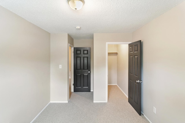 unfurnished bedroom with light colored carpet, a spacious closet, a textured ceiling, and a closet