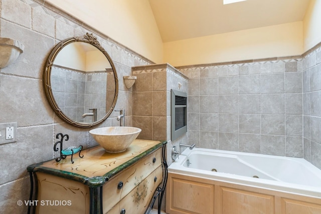 bathroom featuring a washtub, vanity, vaulted ceiling, and tile walls