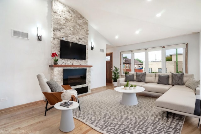 living room featuring a stone fireplace, light hardwood / wood-style flooring, and vaulted ceiling