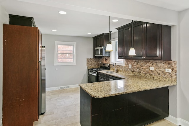 kitchen with kitchen peninsula, light stone countertops, appliances with stainless steel finishes, sink, and pendant lighting