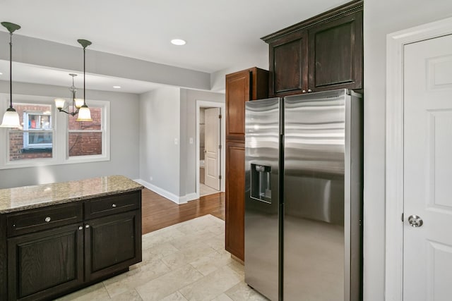 kitchen featuring pendant lighting, light stone counters, stainless steel fridge with ice dispenser, and dark brown cabinetry