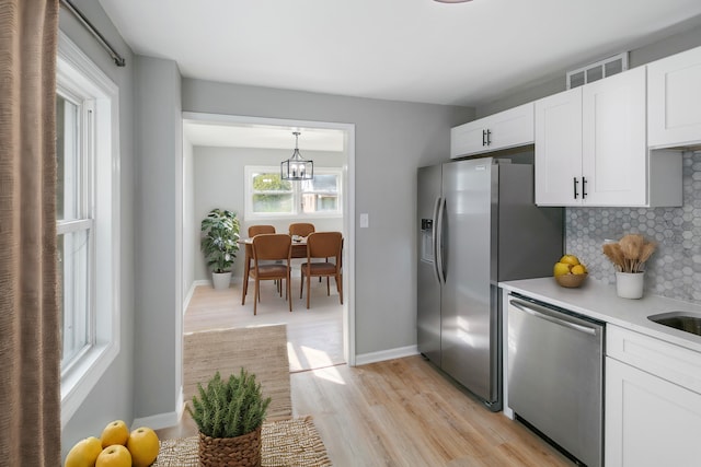 kitchen with appliances with stainless steel finishes, tasteful backsplash, white cabinetry, hanging light fixtures, and light wood-type flooring