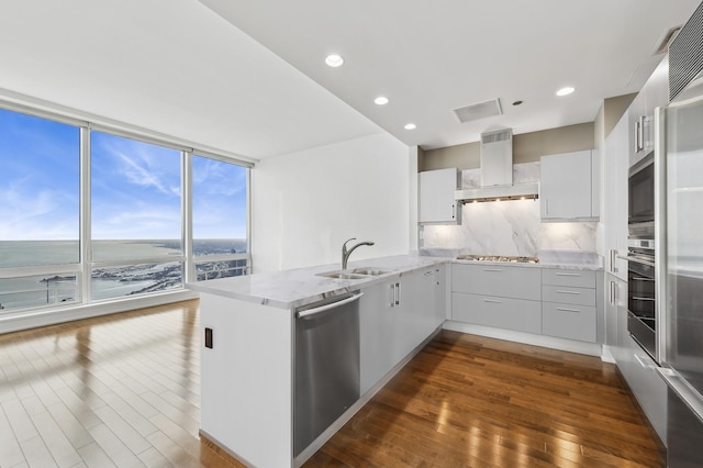 kitchen with appliances with stainless steel finishes, sink, wall chimney range hood, and kitchen peninsula