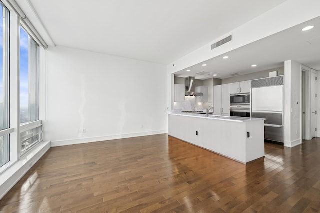 kitchen featuring dark wood-type flooring, white cabinetry, built in appliances, kitchen peninsula, and wall chimney exhaust hood