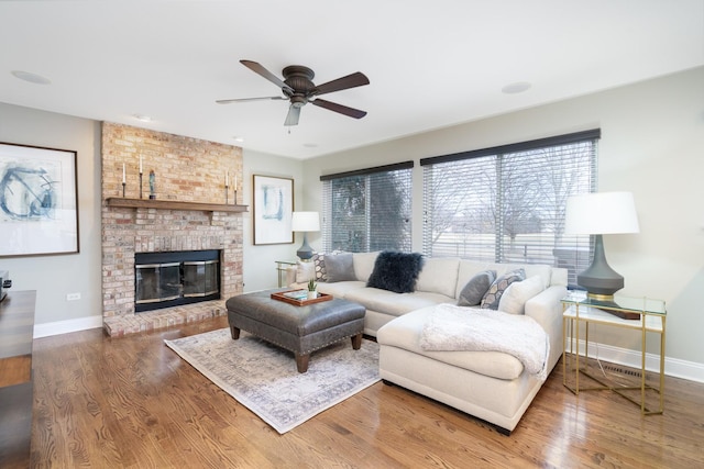 living room featuring ceiling fan, hardwood / wood-style floors, and a brick fireplace