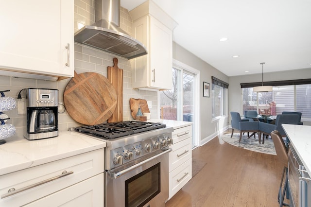 kitchen featuring stainless steel stove, wall chimney exhaust hood, dark hardwood / wood-style floors, decorative backsplash, and light stone countertops