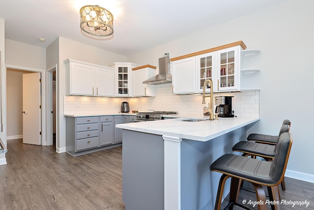 kitchen featuring kitchen peninsula, wall chimney exhaust hood, gray cabinetry, a breakfast bar, and white cabinetry