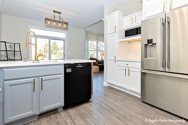 kitchen featuring stainless steel appliances, sink, light hardwood / wood-style flooring, white cabinetry, and hanging light fixtures