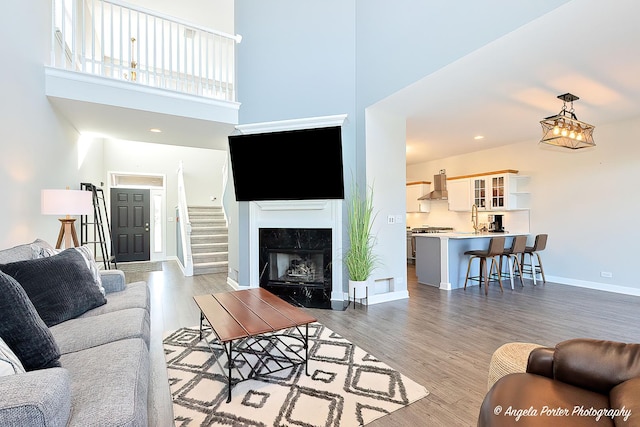 living room featuring a high end fireplace, light hardwood / wood-style flooring, a towering ceiling, and sink