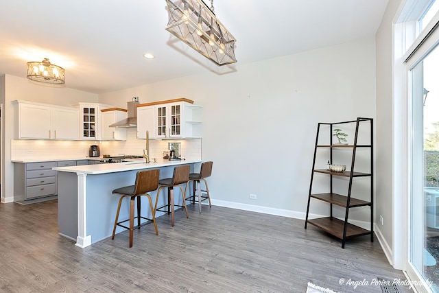 kitchen with backsplash, a kitchen breakfast bar, kitchen peninsula, wall chimney exhaust hood, and white cabinetry