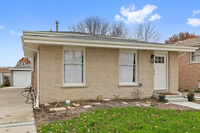 view of front of house with entry steps, an outbuilding, brick siding, and a shingled roof