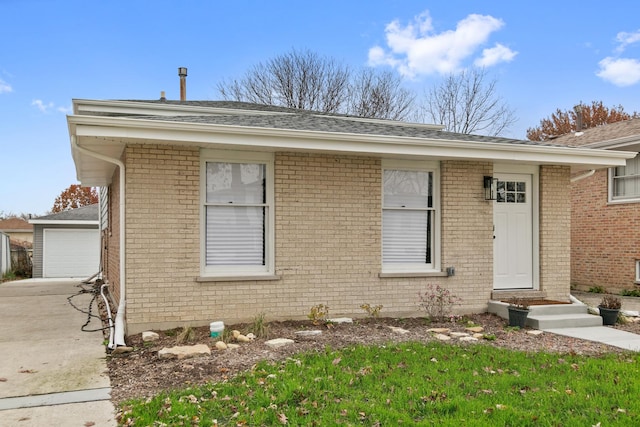 view of front of house with entry steps, an outbuilding, brick siding, and a shingled roof