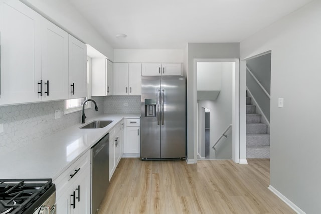 kitchen with appliances with stainless steel finishes, backsplash, sink, light hardwood / wood-style flooring, and white cabinets