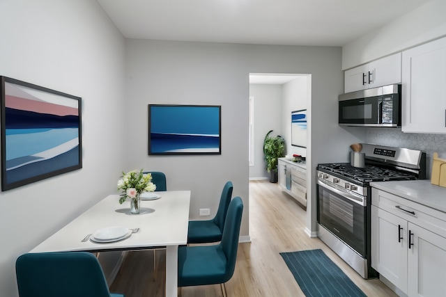 kitchen featuring decorative backsplash, white cabinetry, stainless steel appliances, and light hardwood / wood-style flooring