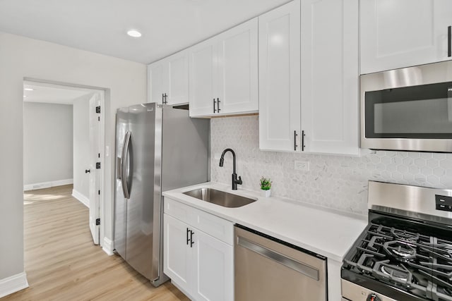 kitchen with backsplash, white cabinets, sink, light wood-type flooring, and appliances with stainless steel finishes