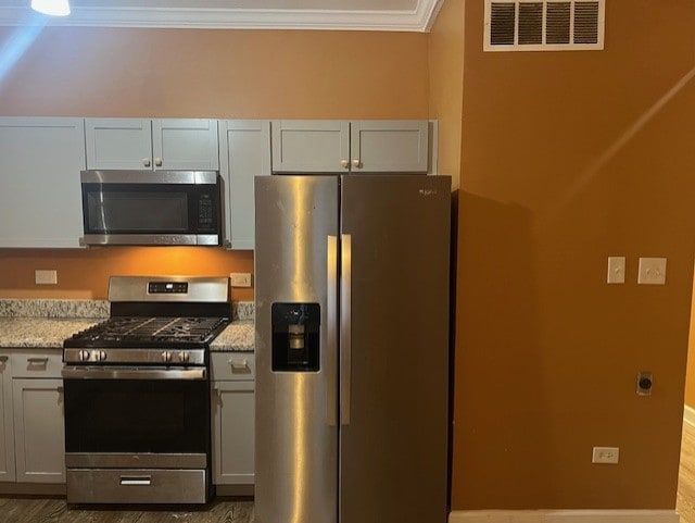 kitchen with appliances with stainless steel finishes, hardwood / wood-style flooring, light stone counters, and crown molding