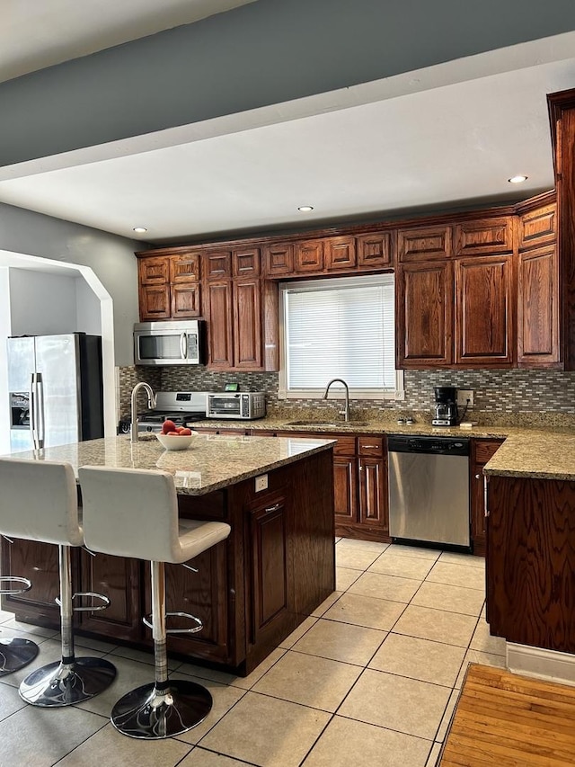 kitchen with a breakfast bar area, an island with sink, light tile patterned floors, and appliances with stainless steel finishes