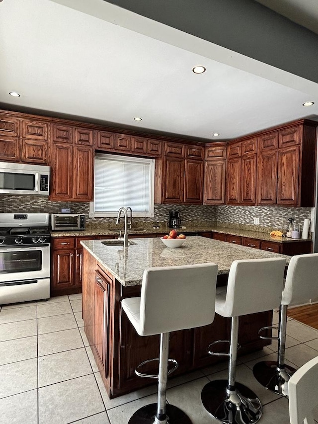 kitchen featuring light stone countertops, sink, a kitchen bar, a center island with sink, and appliances with stainless steel finishes