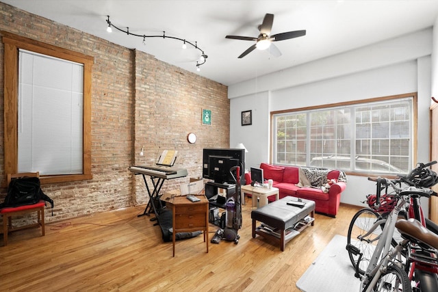 exercise area featuring ceiling fan, light hardwood / wood-style flooring, and brick wall