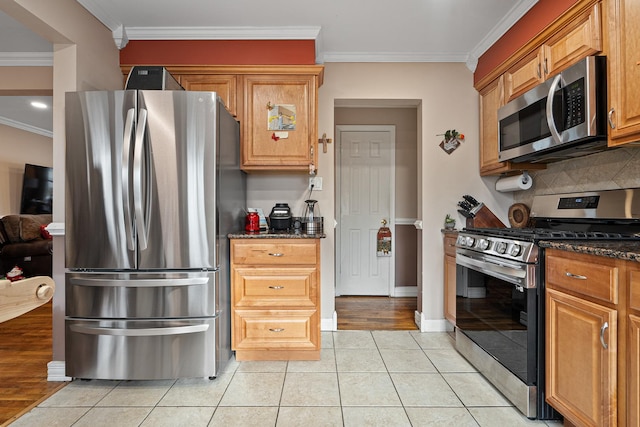 kitchen with dark stone counters, crown molding, decorative backsplash, light tile patterned floors, and stainless steel appliances