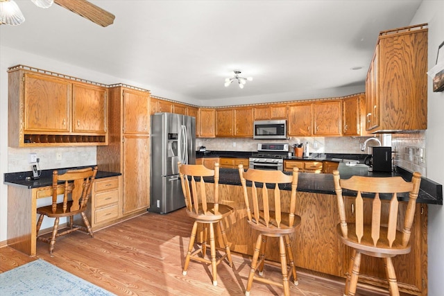 kitchen with a breakfast bar, sink, appliances with stainless steel finishes, tasteful backsplash, and light hardwood / wood-style floors