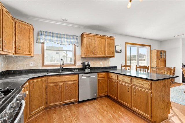 kitchen with sink, stainless steel appliances, backsplash, kitchen peninsula, and light wood-type flooring