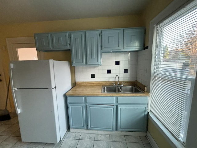 kitchen featuring light tile patterned flooring, backsplash, white fridge, and sink