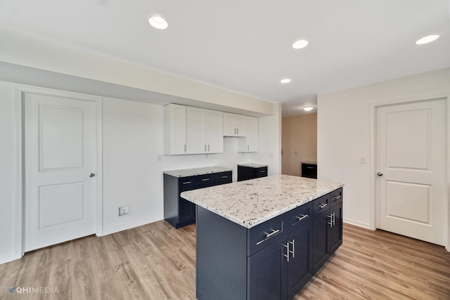 kitchen featuring light stone countertops, light wood-type flooring, blue cabinets, white cabinets, and a kitchen island