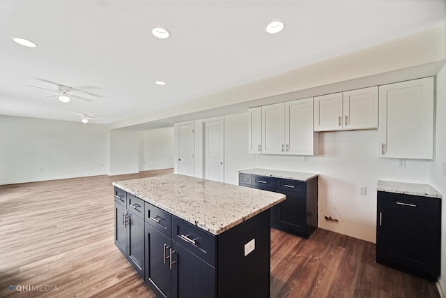 kitchen with light stone counters, ceiling fan, dark wood-type flooring, white cabinets, and a kitchen island