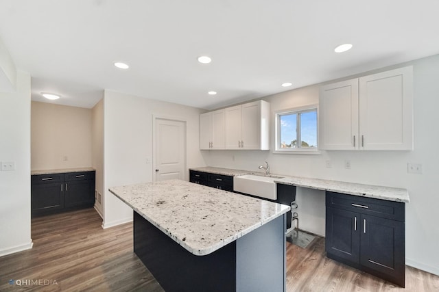 kitchen with sink, hardwood / wood-style flooring, light stone countertops, a kitchen island, and white cabinetry