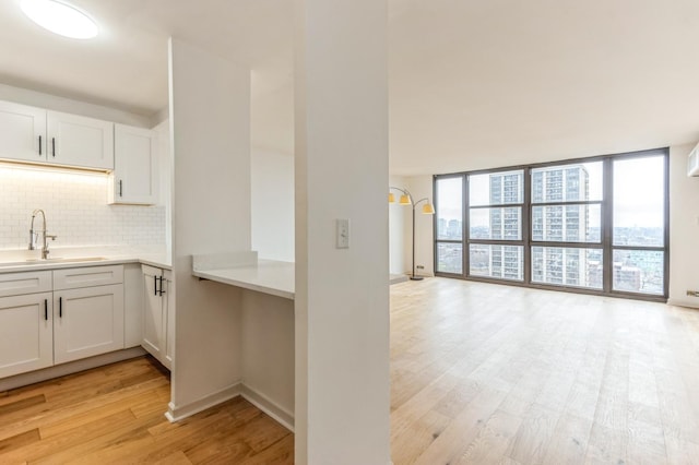 kitchen featuring white cabinets, light wood-type flooring, a wall of windows, and sink