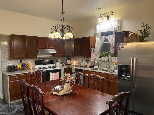 kitchen featuring light stone countertops, stainless steel refrigerator with ice dispenser, sink, pendant lighting, and white range with gas stovetop