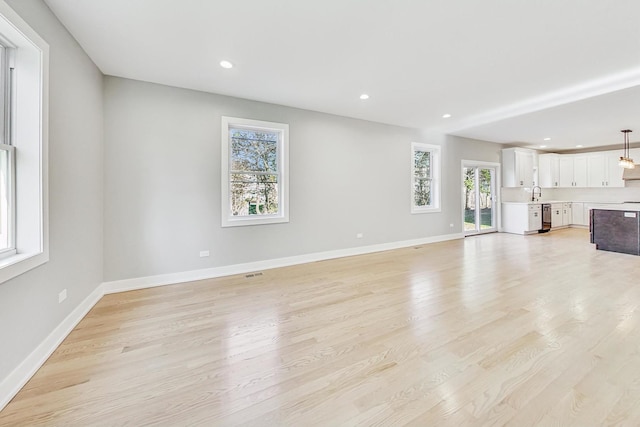 unfurnished living room with light hardwood / wood-style floors, sink, and a wealth of natural light