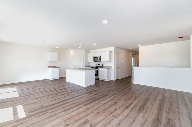 kitchen with white cabinets, appliances with stainless steel finishes, light hardwood / wood-style floors, and a kitchen island with sink