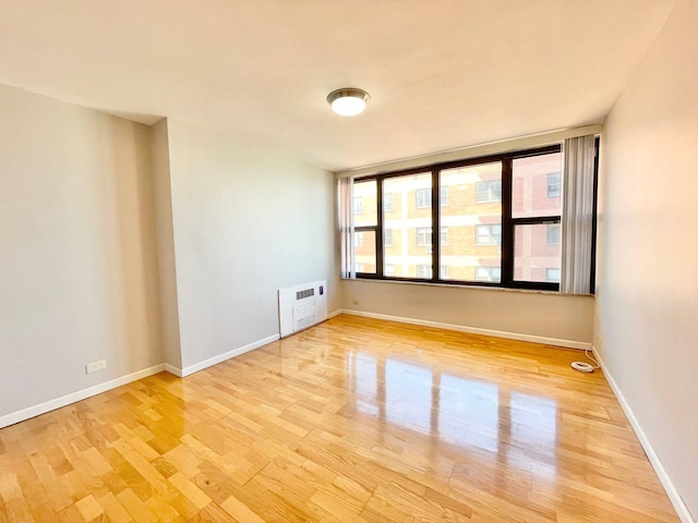 empty room featuring heating unit, light hardwood / wood-style flooring, and a healthy amount of sunlight