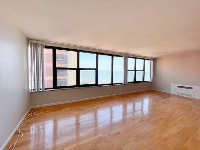 unfurnished room with light wood-type flooring, a water view, heating unit, and a wealth of natural light