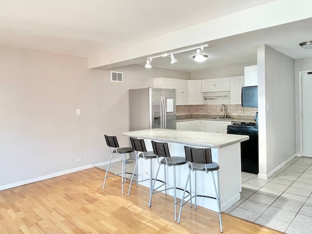 kitchen with white cabinets, decorative backsplash, a kitchen bar, and stainless steel fridge with ice dispenser