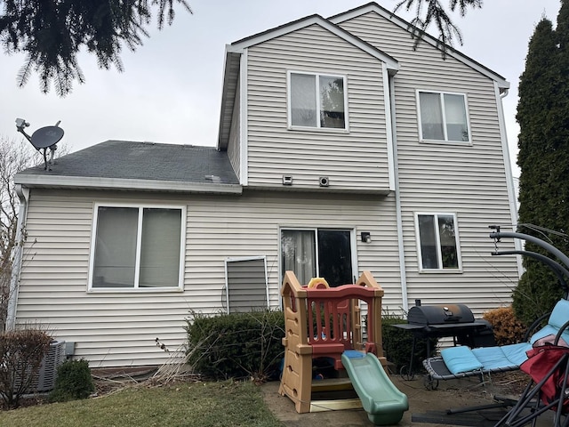 back of house with a playground and central AC unit