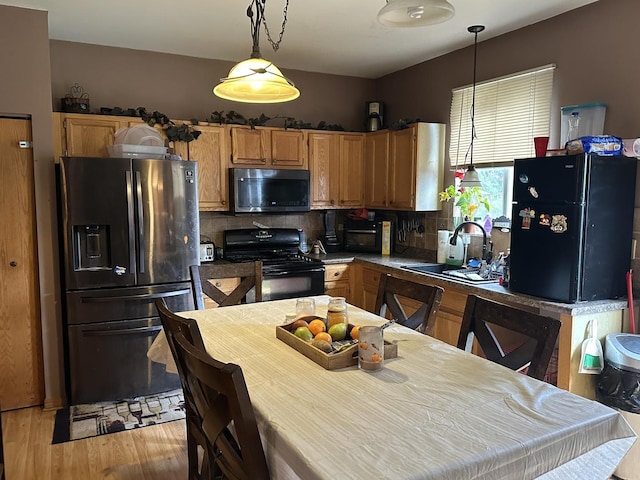 kitchen featuring sink, backsplash, pendant lighting, black appliances, and light wood-type flooring