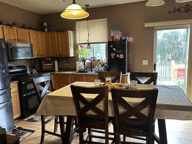 kitchen featuring sink, hanging light fixtures, tasteful backsplash, black appliances, and light wood-type flooring