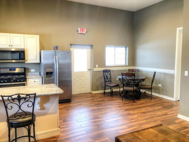 kitchen with dark wood-type flooring, stainless steel appliances, light stone counters, a kitchen bar, and white cabinets