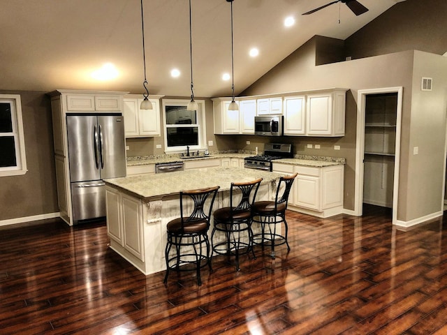 kitchen featuring pendant lighting, white cabinets, a kitchen island, light stone counters, and stainless steel appliances