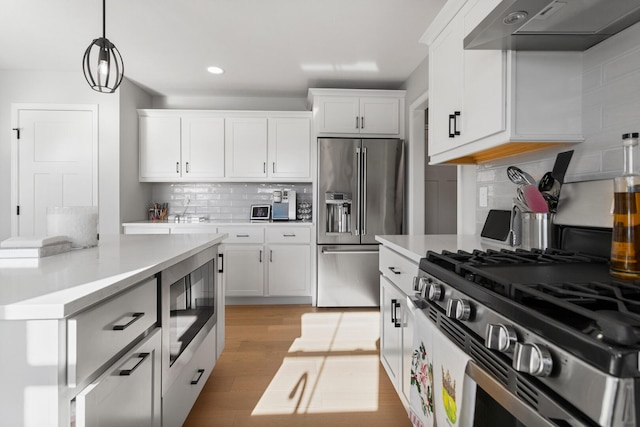 kitchen with stainless steel appliances, white cabinetry, ventilation hood, and hanging light fixtures