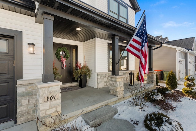 snow covered property entrance featuring a garage and a porch