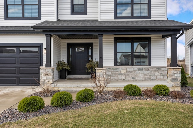 507 Wheatley Dr, Mahomet, IL 61853 - view of exterior entry featuring an attached garage, a shingled roof, stone siding, and a porch