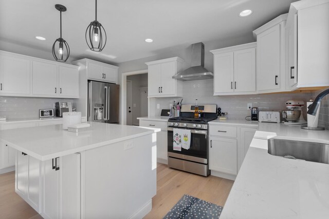 kitchen with stainless steel appliances, wall chimney range hood, hanging light fixtures, and white cabinetry