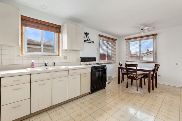 kitchen with white cabinetry, sink, ceiling fan, black gas range oven, and decorative backsplash