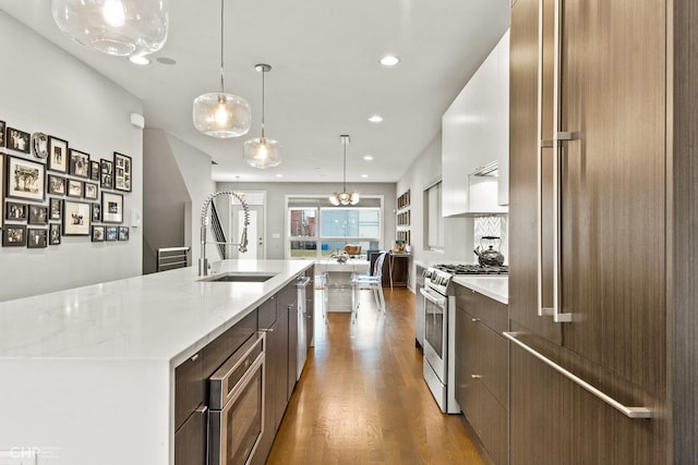 kitchen with dark wood-type flooring, hanging light fixtures, light stone counters, a large island with sink, and appliances with stainless steel finishes