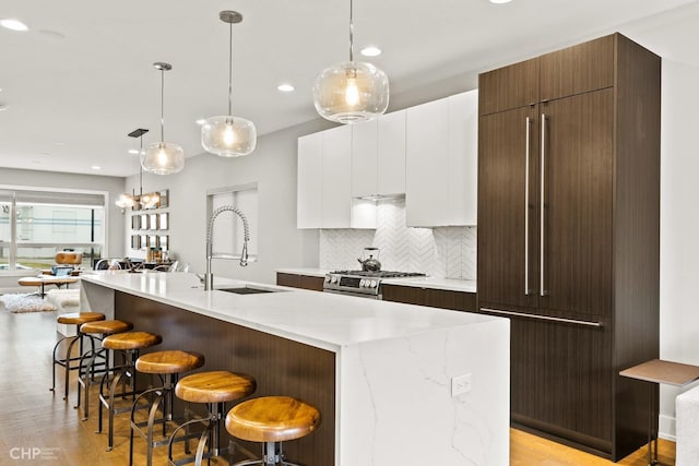 kitchen featuring white cabinets, a center island with sink, sink, gas range, and a kitchen bar